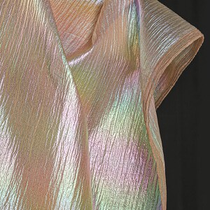 May include: Iridescent fabric with a textured, rippled surface. The fabric displays a spectrum of colors, including pink, yellow, and green, creating a shimmering effect. The material is folded, suggesting it could be used for clothing or decorative purposes.