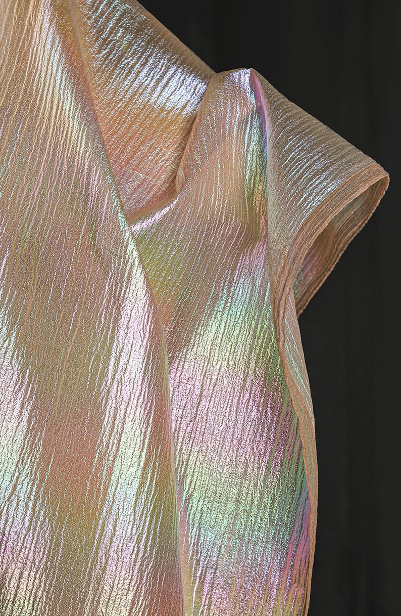 May include: Iridescent fabric with a textured, rippled surface. The fabric displays a spectrum of colors, including pink, yellow, and green, creating a shimmering effect. The material is folded, suggesting it could be used for clothing or decorative purposes.