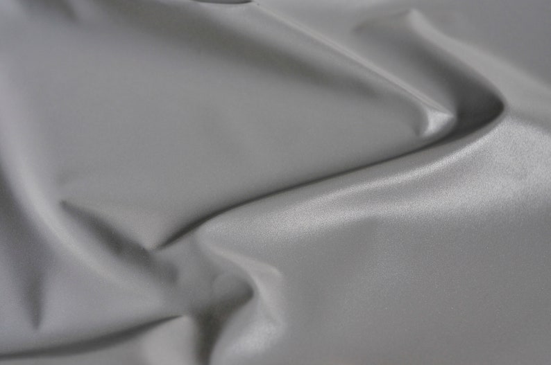 May include: A close-up of a smooth, gray fabric with a subtle sheen. The fabric is draped and folded, creating soft, flowing lines.