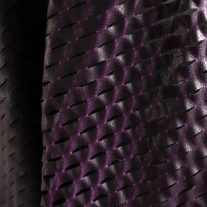 Puede incluir: Un material de color morado oscuro con una superficie texturizada similar al cuero, que presenta un patr&oacute;n repetitivo de cortes horizontales. Los bordes de estos cortes revelan un tono morado brillante, creando una apariencia dimensional.