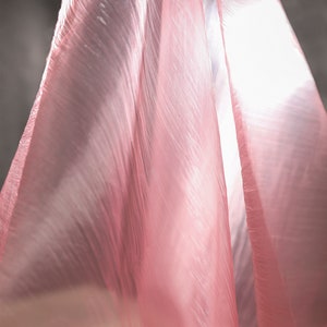 May include: A sheer pink fabric with a crinkled texture, draped and flowing in a soft, light way.