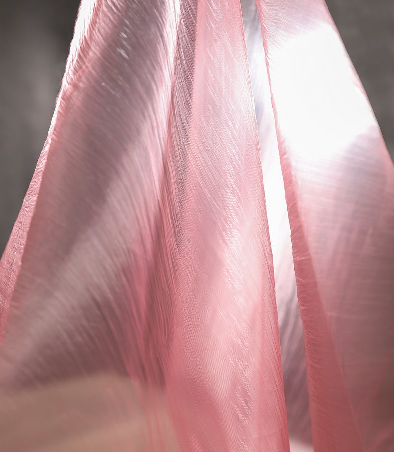 May include: A sheer pink fabric with a crinkled texture, draped and flowing in a soft, light way.