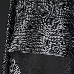 May include: Close-up of a black and white woven fabric with a textured pattern. The fabric appears to be layered, with a contrasting black material visible underneath. The weave creates a dynamic, three-dimensional effect.