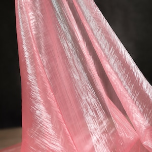 May include: Pink sheer fabric with a crinkled texture. The fabric is draped and folded, creating a soft, flowing look.