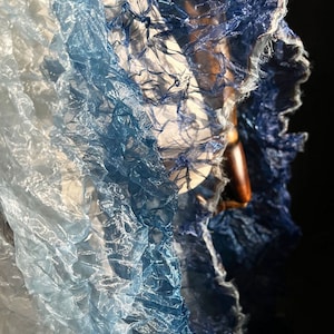 Puede incluir: Una tela azul y blanca degradada con una textura arrugada. La tela es transparente y delicada, con un suave y fluido drapeado.