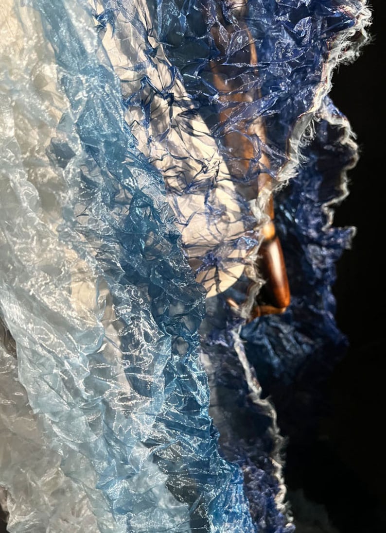 Puede incluir: Una tela azul y blanca degradada con una textura arrugada. La tela es transparente y delicada, con un suave y fluido drapeado.