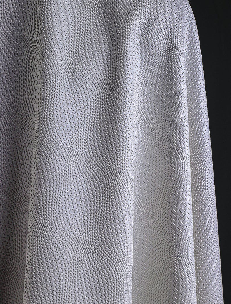 May include: Close-up of a white fabric with a woven texture. The fabric is draped, creating soft waves and shadows. The weave pattern is consistent throughout, giving a sense of depth and dimension. The material appears to be smooth and possibly synthetic.