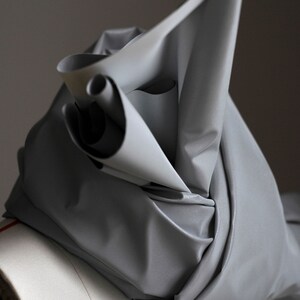 May include: A silver fabric draped over a white mannequin form. The fabric is folded and twisted, creating a unique and abstract shape.