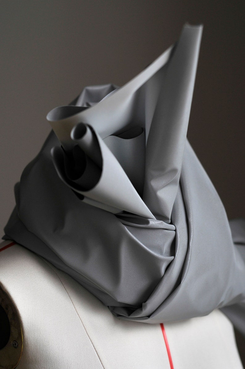 May include: A silver fabric draped over a white mannequin form. The fabric is folded and twisted, creating a unique and abstract shape.