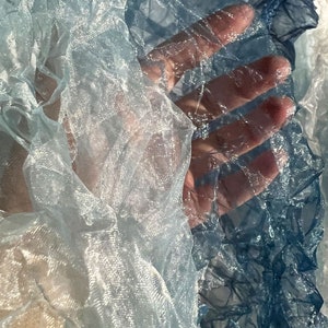 Puede incluir: Primer plano de una tela transparente y arrugada en tonos azules y blancos. La tela es transl&uacute;cida y tiene una calidad delicada y et&eacute;rea.