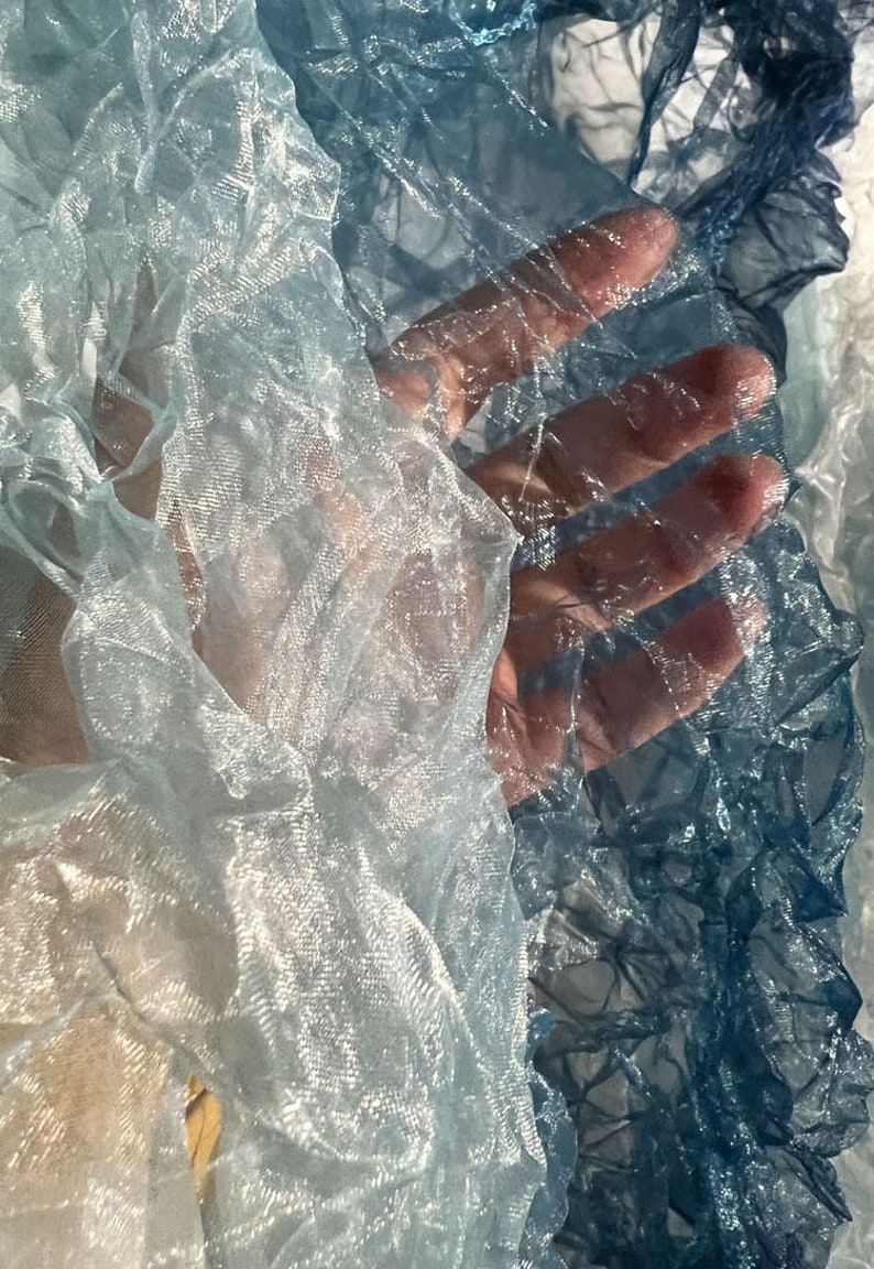 Puede incluir: Primer plano de una tela transparente y arrugada en tonos azules y blancos. La tela es transl&uacute;cida y tiene una calidad delicada y et&eacute;rea.