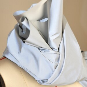 May include: A silver reflective fabric draped over a dress form. The fabric is folded and bunched up, creating a soft, flowing look.