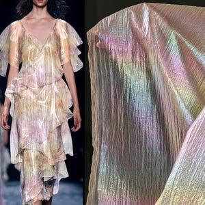 May include: A shimmering, iridescent fabric and a layered dress. The fabric has a textured appearance with a rainbow sheen. The dress features a V-neckline and layered ruffles, creating a flowing silhouette. The colors include pastel shades of pink, yellow, and green.