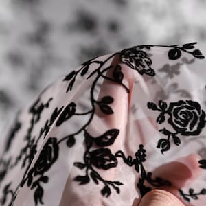 May include: Black floral embroidery on sheer white fabric. The fabric is delicate and has a soft, flowing texture.