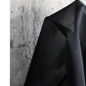 May include: Black sheer fabric with a smooth texture. The fabric is draped over a textured surface.