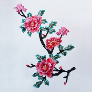 以下が含まれることがあります： 黒い茎にピンクと赤の花と緑の葉が付いた刺繍された花のアップリケです。