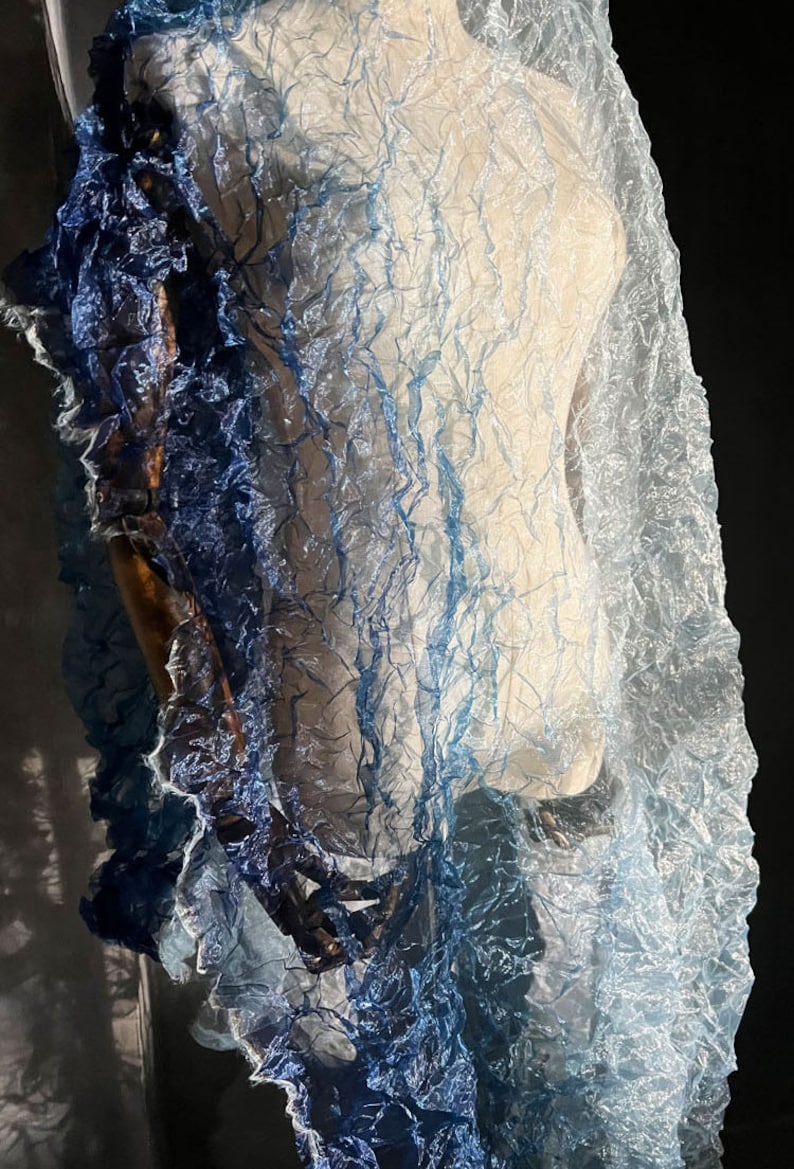 Puede incluir: Una bufanda transparente de color azul y blanco degradado con textura arrugada. La bufanda est&aacute; drapeada sobre un maniqu&iacute;.