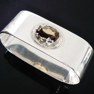 May include: A white ceramic mug with a black handle and the text "But First, Coffee" in a black, handwritten-style font. The mug is on a white surface.