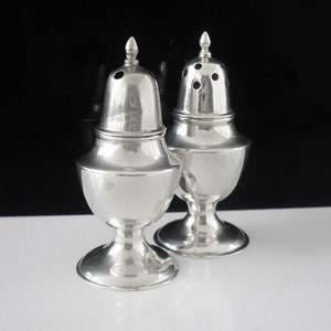 May include: Two silver salt and pepper shakers with a classic design. The shakers have a round body with a domed top and a small base.