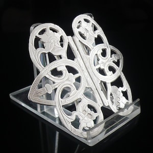 May include: A pair of silver bookends in the shape of a butterfly. The bookends are intricately designed with floral patterns and are made of a delicate, openwork style.