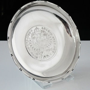 May include: A silver plate with a raised design of a coat of arms featuring a double-headed eagle and the text "BRVNC. COL. ARCHID. AVST. DUX."