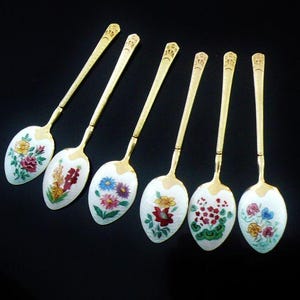 以下が含まれることがあります： 白の柄と花柄の金メッキティースプーン6本セット。各スプーンには、赤、ピンク、黄、緑、青の色合いの異なる花柄が施されています。