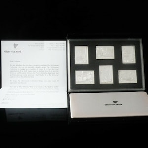 May include: A black box with a white interior containing six silver commemorative stamps. The stamps feature images of buildings and the text "Hibernia Mint".