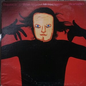 May include: A vinyl record cover with a red background and a black silhouette of a person wearing a mask. The mask is yellow with blue eyes and a red mouth. The text "Happiness", "Brian Auger's Oblivion Express", and "Heart aches" is printed on the cover.