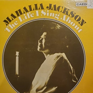 May include: A yellow vinyl record album cover featuring a black and white photo of Mahalia Jackson singing. The album title is "The Life I Sing About" and the text "CAEDI" is in the top right corner.