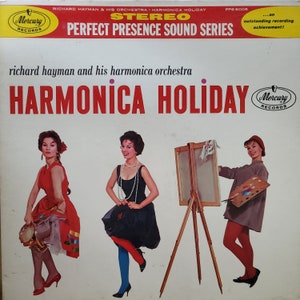 May include: Vintage vinyl record album cover for "Harmonica Holiday" by Richard Hayman and his harmonica orchestra. The cover features three women in colorful dresses, one holding a tambourine, another with a pearl necklace, and the third with a painter's palette.