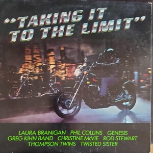 May include: Album cover with the text "TAKING IT TO THE LIMIT" in silver and green. Two motorcycles are shown in front of a city skyline at night. The album features Laura Branigan, Phil Collins, Genesis, and others.