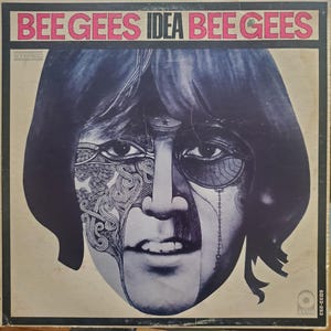 May include: Vintage vinyl record album cover for the Bee Gees' "Idea." The album art features a stylized face with intricate designs on one side and the band's name in pink and black lettering at the top. The album is a stereo recording.
