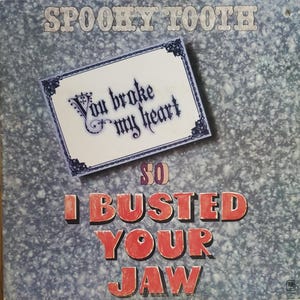 May include: Album cover for Spooky Tooth featuring the text "You broke my heart" and "So I busted your jaw." The text is in various fonts and colors against a textured, gray background.