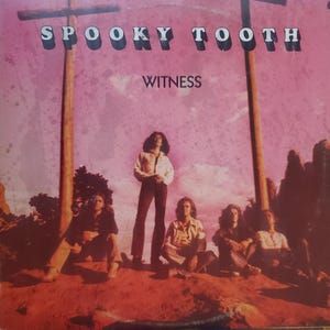 May include: Album cover for Spooky Tooth's "Witness" featuring the band members in a desert landscape. The album title is in large, bold letters at the top, with the word "Witness" below. The background is a pink and purple sky.