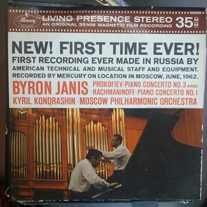 May include: A vintage record album cover featuring a black and white photo of two men playing a piano in a concert hall. The album cover is titled "New! First Time Ever!" and features the names "Byron Janis" and "Kyril Kondrashin" along with the text "Prokofiev-Piano Concerto No. 3 and Rachmaninoff-Piano Concerto No. 1".