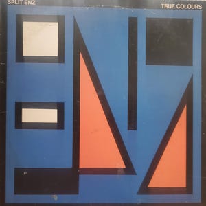 May include: Album cover for Split Enz's "True Colours." The design features a blue background with black geometric shapes and orange triangles. The band's name is at the top left, and the album title is at the top right.