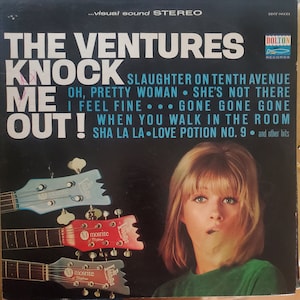 May include: A vintage vinyl record album cover featuring The Ventures, a popular instrumental rock band. The cover features a woman with blonde hair and a green shirt, and three guitars with the word "Ventures" on the headstock. The album title is "Knock Me Out!" and includes a list of songs, including "Slaughter on Tenth Avenue", "Oh, Pretty Woman", "She's Not There", "I Feel Fine", "Gone Gone Gone", "When You Walk in the Room", and "Sha La La Love Potion No. 9".