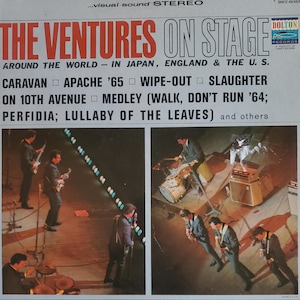 May include: Vintage album cover for "The Ventures On Stage." The cover features a red and white title with a list of songs. The image shows the band performing live, with musicians playing guitars and drums on a stage.
