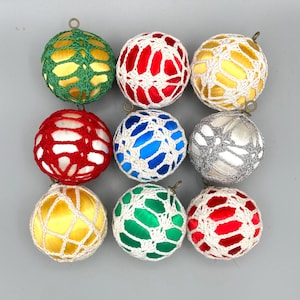 May include: A set of nine spherical ornaments, each featuring a smooth, satin-like core in various colors including red, blue, green, yellow, and silver, encased in a decorative, open-work crochet netting with a small metal hanging loop.