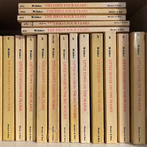 May include: A collection of vintage books by Wilder, including titles like "Little House on the Prairie" and "The First Four Years." The books have cream-colored covers with red and black text, arranged on a shelf. The spines display the author's name and series title.