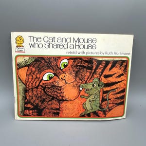 May include: A vintage children's book titled "The Cat and Mouse Who Shared a House." The cover features a large orange cat with green eyes and a small green mouse. The book is retold with pictures by Ruth Hürlimann.