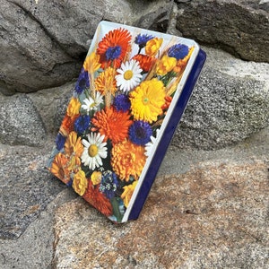 May include: A vintage tin box with a blue border and a colorful floral design. The flowers are yellow, orange, white, and blue.