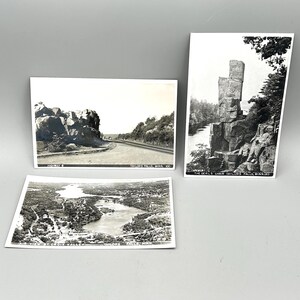 May include: Three vintage black and white postcards featuring scenic views. One shows a road and rock formations, another depicts a tall rock structure, and the third offers an aerial view of a lake and town. Each postcard has text.