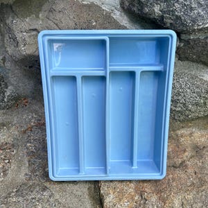 May include: A light blue plastic cutlery tray with multiple compartments. The tray is rectangular with a raised edge and is designed to organize silverware. The compartments are of varying sizes, suitable for forks, knives, and spoons.