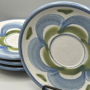 May include: A stack of ceramic plates with a white center and a blue and green floral design. The plates have a slightly textured surface and a blue rim. The design is a repeating pattern of curved shapes in shades of blue and green.