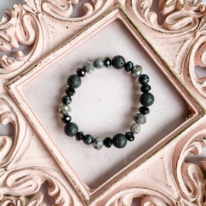 May include: A black and grey beaded bracelet with lava rock beads, silver beads, and a single sparkly silver bead.