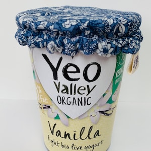 Può includere: Un coperchio in tessuto blu e bianco copre un contenitore di yogurt bianco con il testo "Yeo Valley Organic" e "Vanilla light bio live yogurt".