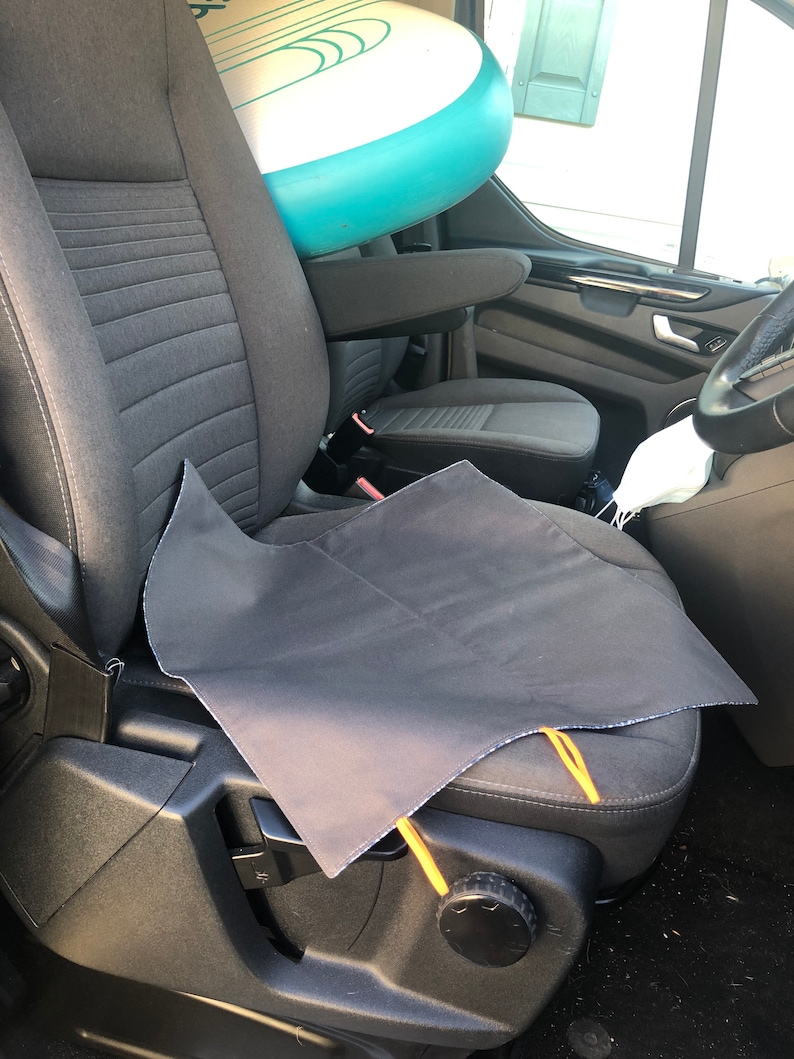 Puede incluir: Una funda de asiento negra con lazos amarillos se coloca sobre un asiento de coche gris. Una tabla de paddle surf inflable blanca y turquesa descansa contra el asiento. Se ve el interior de un veh&iacute;culo.