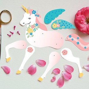 May include: A pink and white paper unicorn with blue wings and flowers. The unicorn is cut out and ready to be assembled. There are also pink flower petals and small gold tacks.