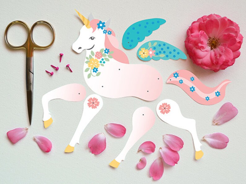 May include: A pink and white paper unicorn with blue wings and flowers. The unicorn is cut out and ready to be assembled. There are also pink flower petals and small gold tacks.